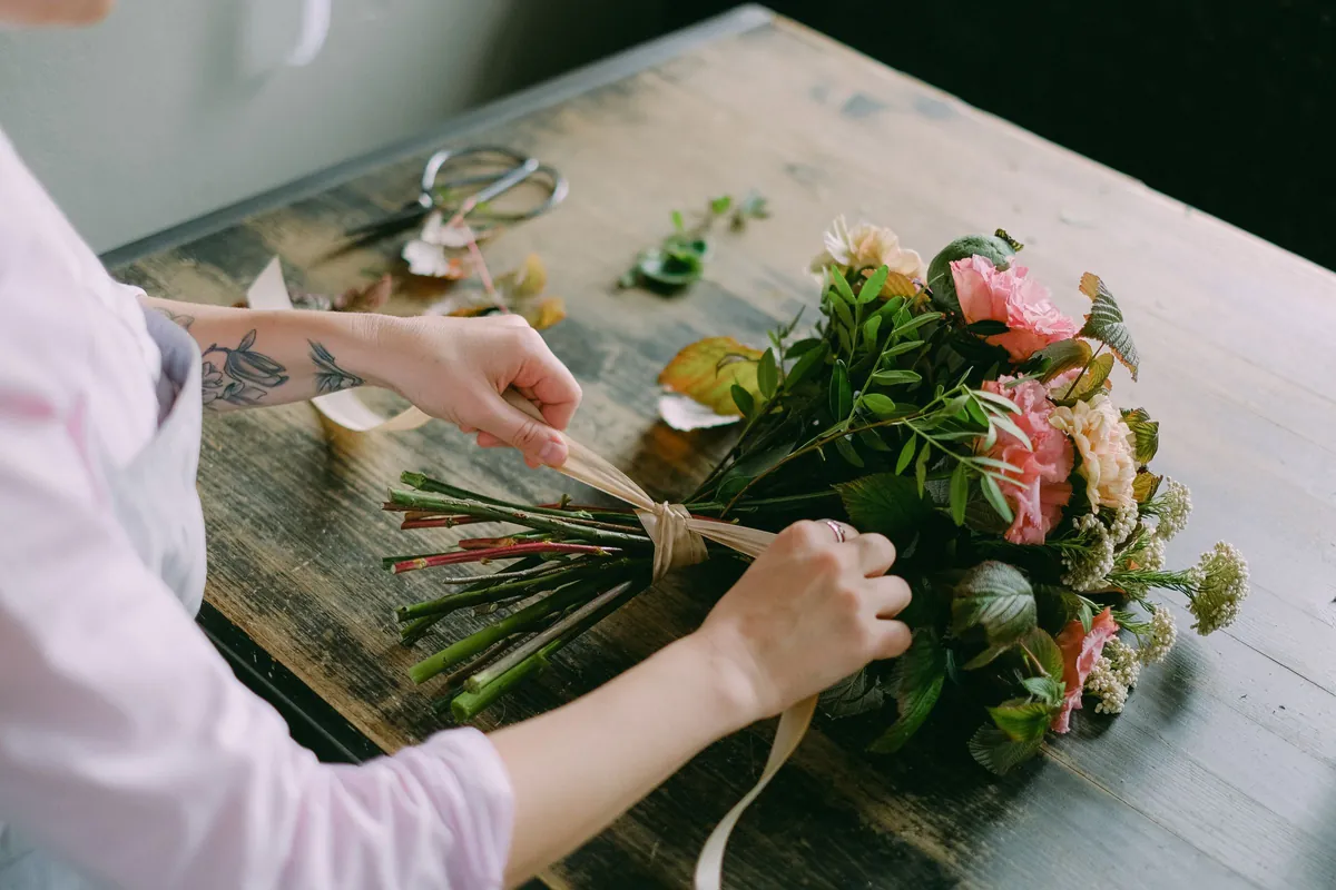 Handen binden een boeket met lint op een houten werktafel